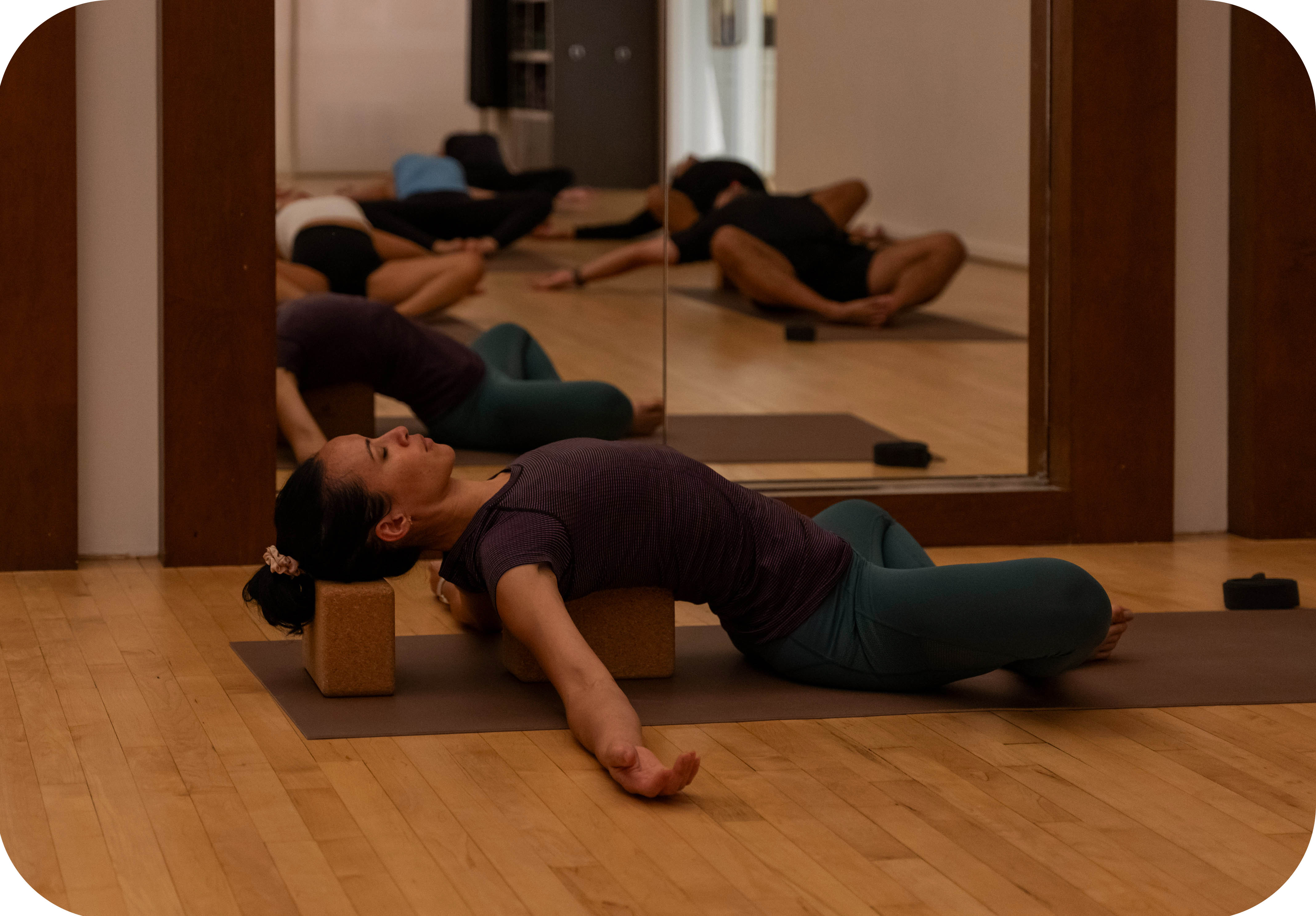 Female yoga instructor laying back over a yoga block doing some breathwork exercises during a yoga class at the Adelaide Club