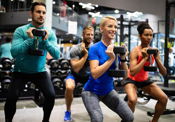 4 young men and women participating in a group fitness weight class in a fitness studio