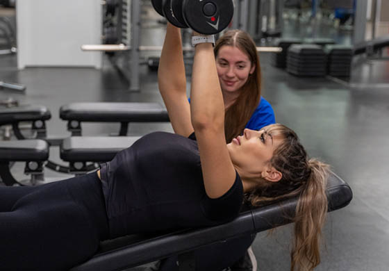 Young, fit woman lifting weights in the Adelaide Club's Women's Gym with a female personal trainer overlooking her